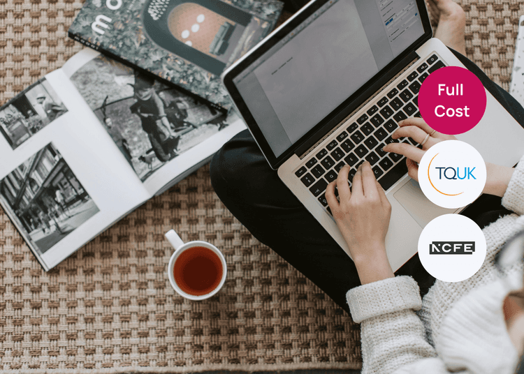 Person typing on a laptop while seated on a patterned floor with books and a cup of tea nearby for digital skills training.