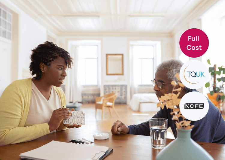 Carer sitting with an older adult at a table, holding a medication blister pack during a discussion about medicines.