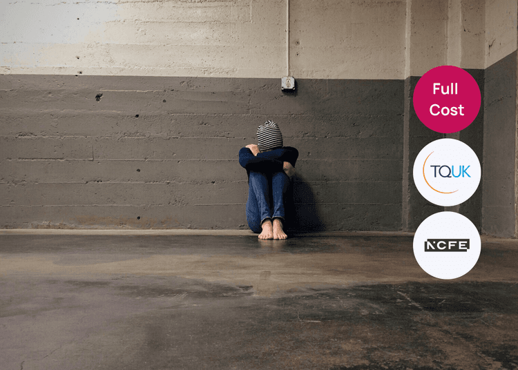Person sitting on the floor in an empty concrete room with knees pulled to their chest, relevant to domestic abuse awareness.