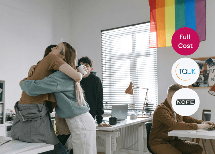 Group of young people in an office, with two hugging near a rainbow pride flag, relating to LGBTQIA+ inclusivity training.