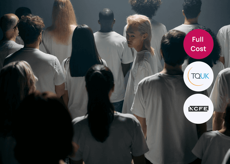 Group of people standing in a dimly lit room wearing white shirts, with one person turning back toward the camera, linked to equality training.