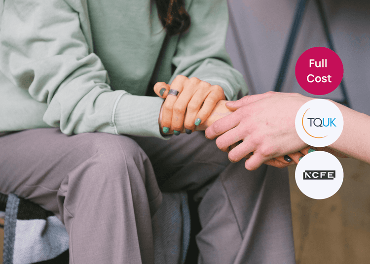 Close up of two people sitting together holding hands in a supportive gesture, suitable for mental health or care training.