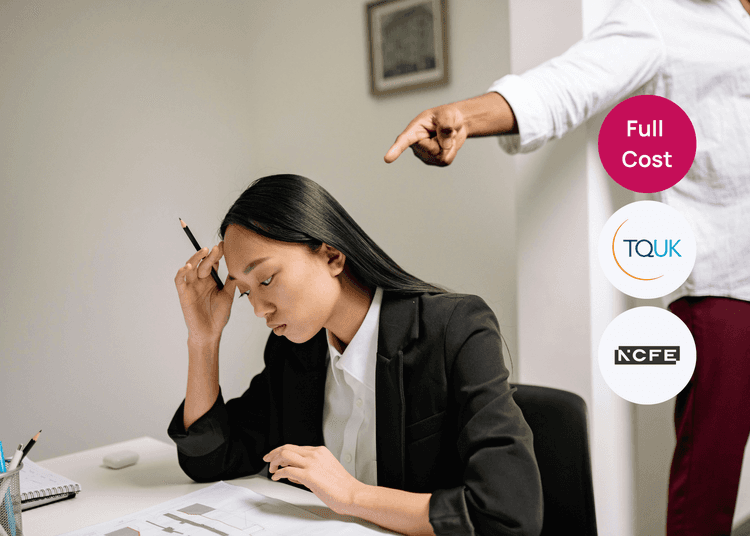 A woman sitting at a desk holding a pencil while someone behind her points toward her in a workplace setting.