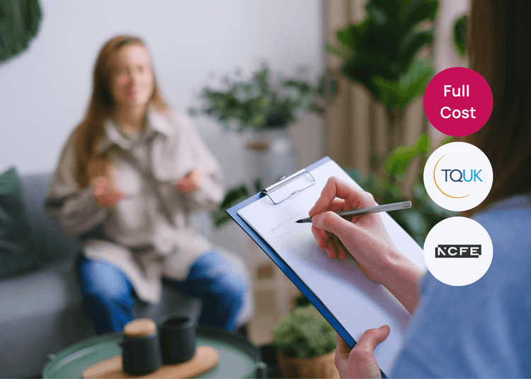 A person holding a clipboard and taking notes while seated across from a woman speaking during a session.