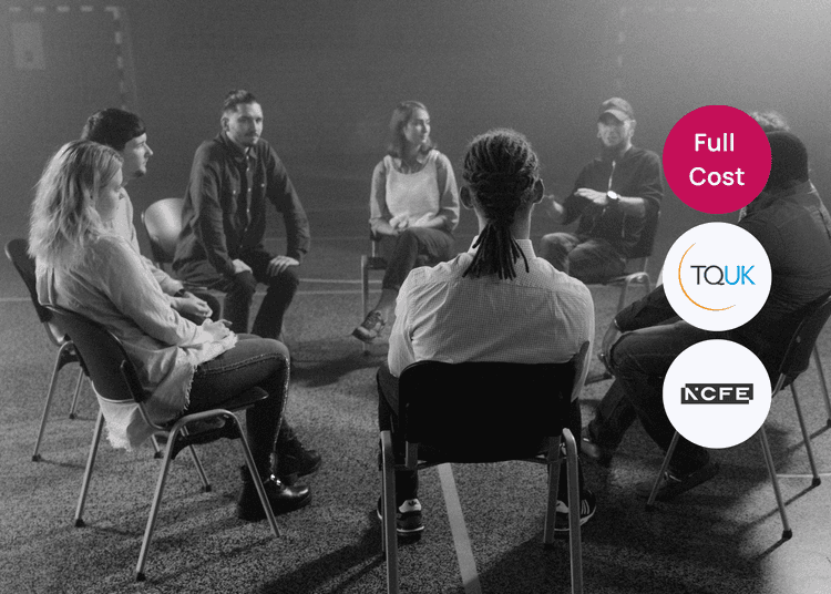 A group of adults seated in a circle during a discussion session in a dimly lit room.