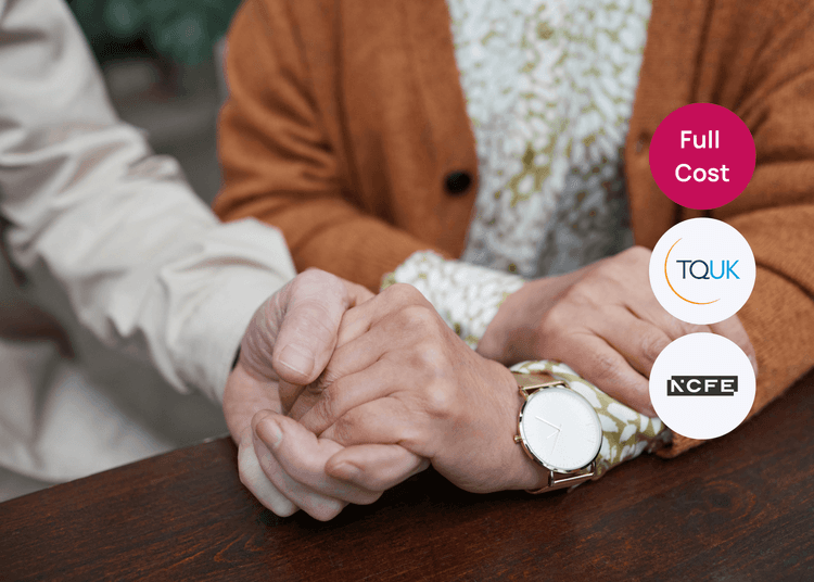 Two people sitting at a table with one person gently holding the hands of an older adult for care training.