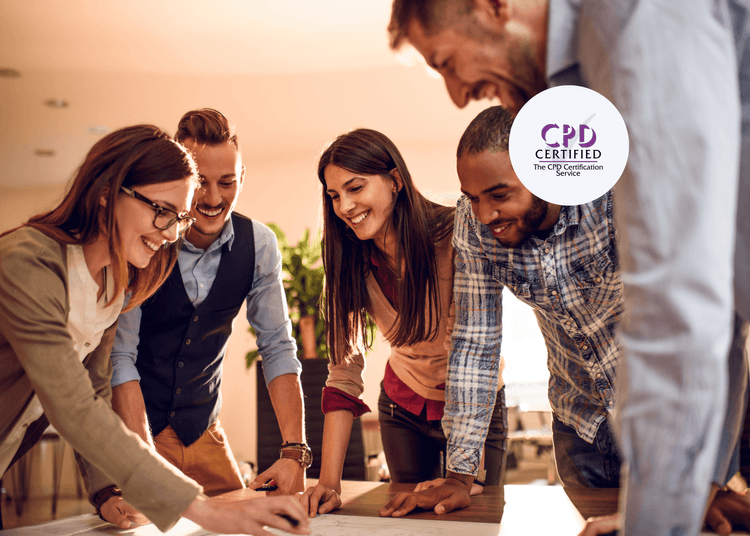 Group of five colleagues smiling and leaning over a desk while working together on a shared project or plan.