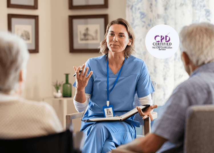 Female nurse in blue scrubs sits with an open notebook, speaking to two older adults in a home setting.