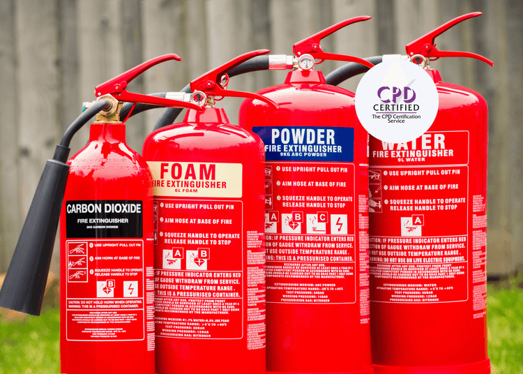 Red fire extinguishers for Carbon Dioxide, Foam, Powder, and Water together in a line shown outside on grass.