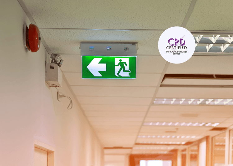 A clearly marked green fire exit sign mounted on the ceiling of a care home, positioned beside the fire alarm for emergency visibility.