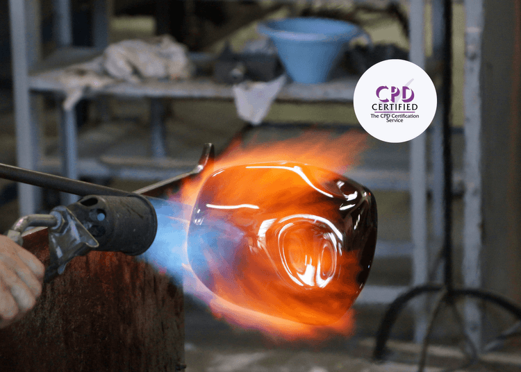 Close-up of a hand using a gas torch to heat a molten glass object, surrounded by orange and blue flames.