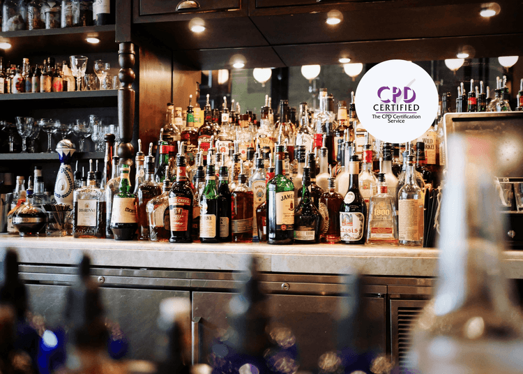 Bar stocked with assorted alcohol bottles in front of a mirrored wall, with shelves of glassware above and behind.