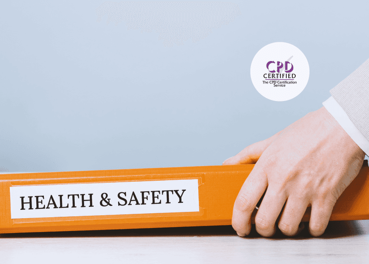 Close-up of a hand holding an orange binder labelled “HEALTH & SAFETY” on a light wooden desk.