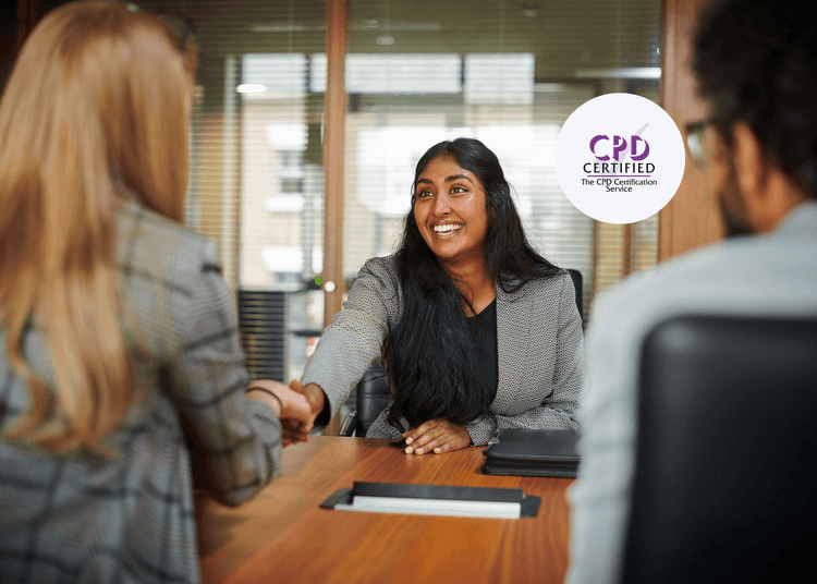Smiling woman in a blazer shaking hands across a meeting table during a job interview with two interviewers.