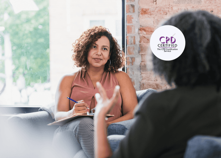 Woman with curly hair holding a pen and clipboard, listening to another person speaking during a seated conversation.