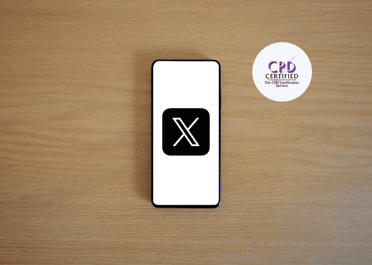 Smartphone on wooden table displaying the black and white “X” logo for the social media platform X (formerly Twitter).