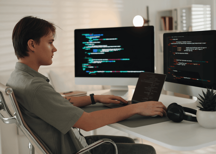 Learner working on coding at a desk with code displayed across multiple computer screens.
