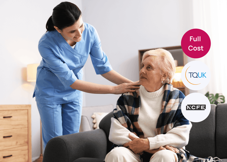 Carer in blue uniform supporting an older woman seated on a sofa in a home care setting.