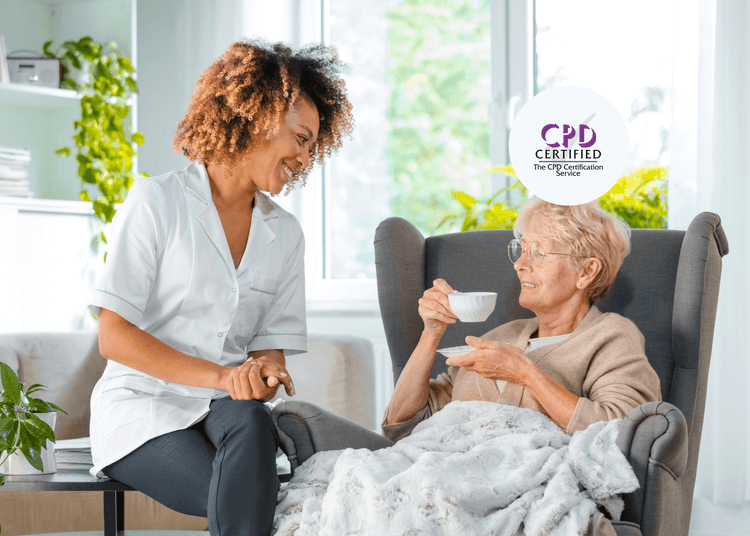 Smiling carer sits beside an older woman drinking tea in a cosy chair, both engaged in friendly conversation.