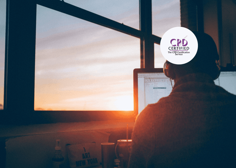 Person wearing headphones working at a desktop computer in front of a large window during a sunset.
