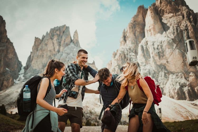 Group of young travellers with backpacks laughing together in a mountain landscape, representing exploration and tourism experiences in the Level 2 Certificate in Travel and Tourism course.