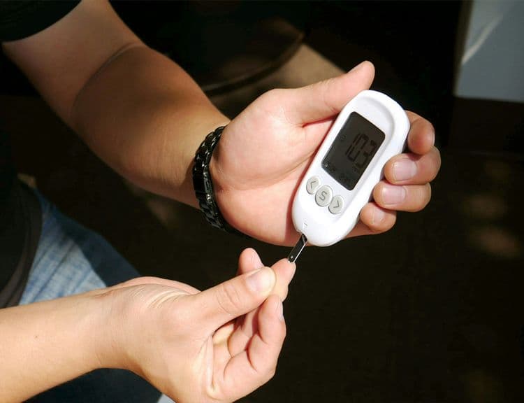Person inserting a test strip into a blood glucose monitor to check blood sugar levels, illustrating monitoring in the Level 3 on Diabetes Management course.