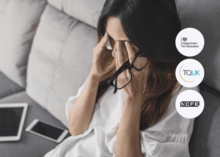 Woman sitting on sofa holding her glasses and rubbing her eyes, with a tablet and phone nearby.