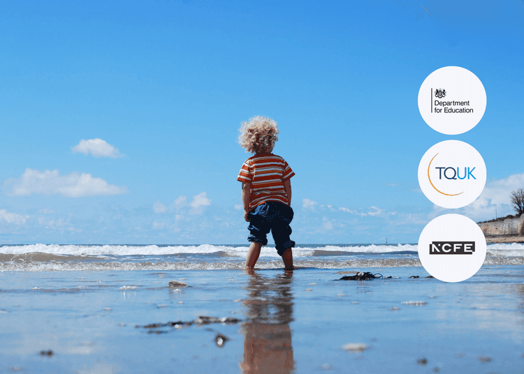 Young child with curly blonde hair in striped shirt standing at the water’s edge on a sandy beach.