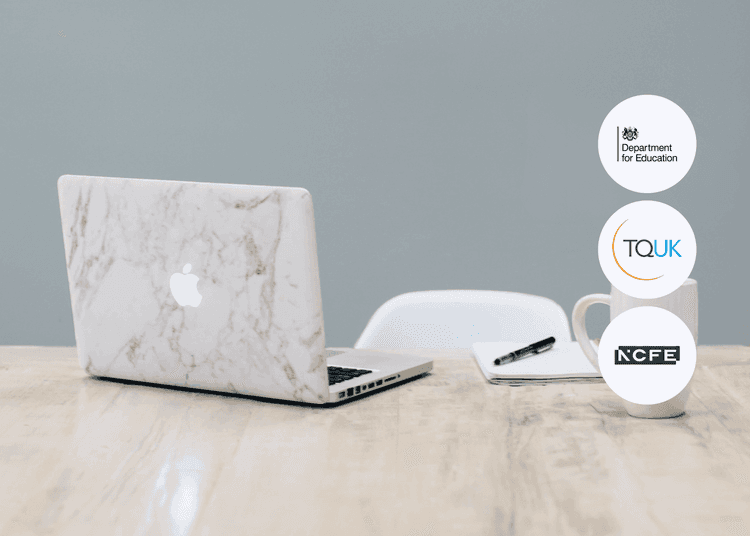 Open laptop with marble cover on a wooden desk next to a mug, notebook, and pen.