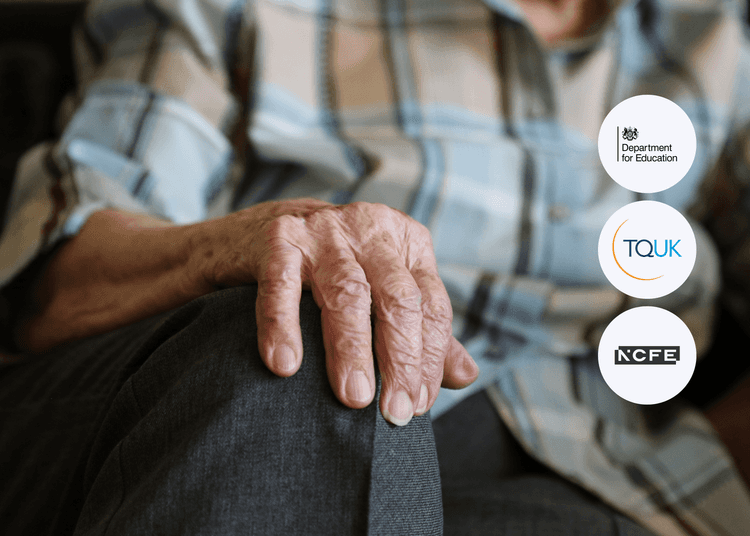 Close-up of an elderly person’s hand resting on their knee, wearing a plaid shirt and dark trousers.