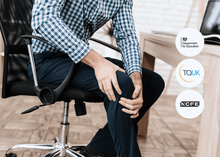 Man in a checked shirt sitting in an office chair, holding his knee with both hands in visible discomfort.