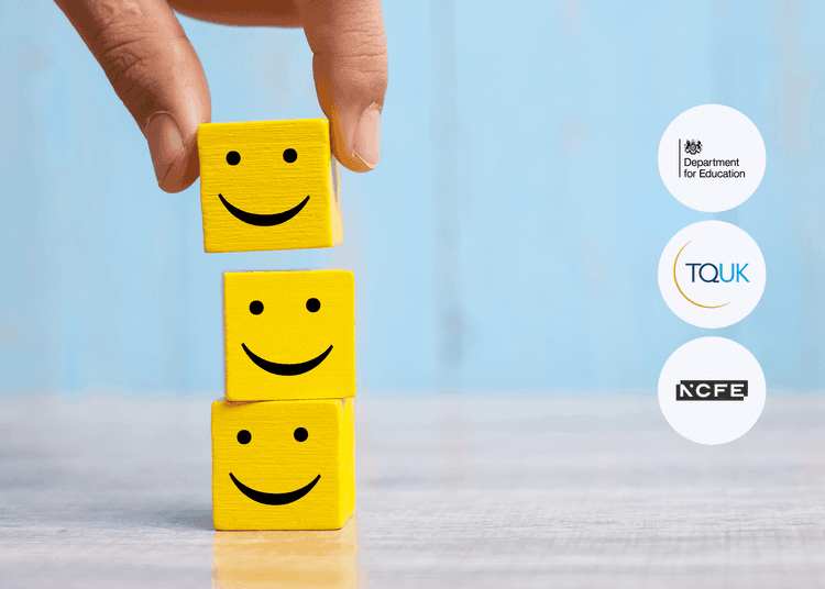Hand placing a yellow wooden block with a smiling face on top of two similar stacked blocks on a wooden surface.
