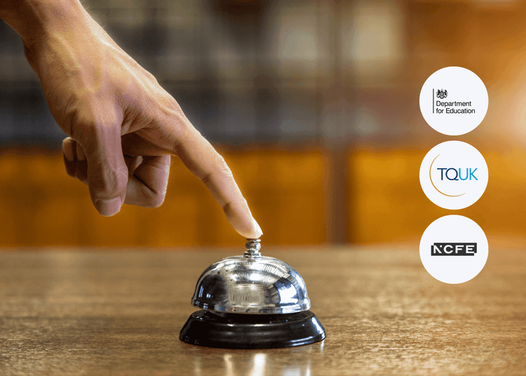 Hand with visible veins pressing a polished silver service bell on a wooden counter in a warmly lit hospitality setting.