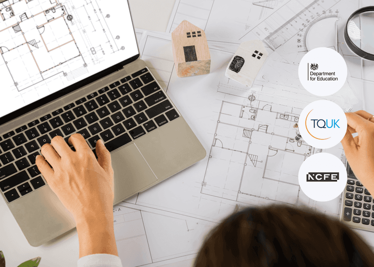 Person using a laptop with architectural drawings on screen, surrounded by floor plans, wooden house models, and tools.