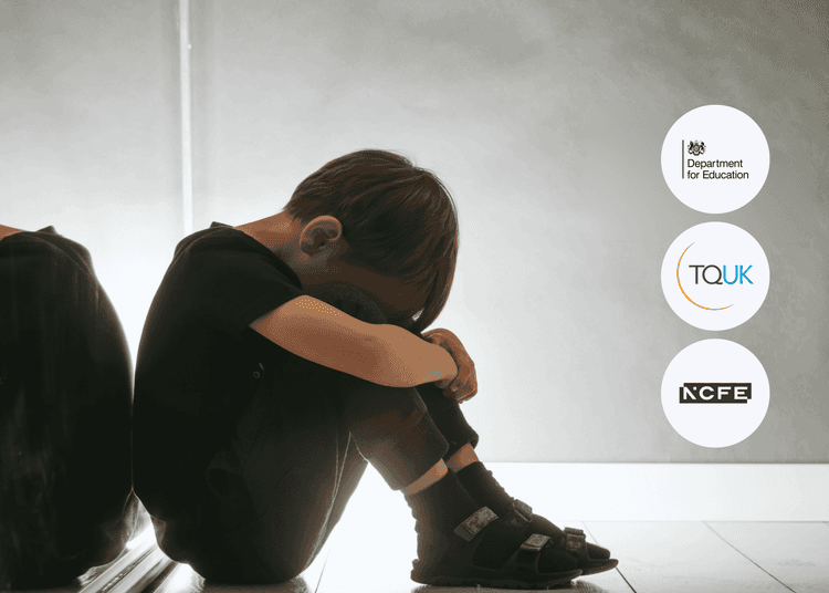 Young child in dark clothing sitting on the floor with head down and arms wrapped around knees beside a wall.