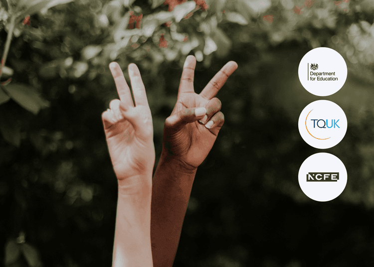 Two raised hands with different skin tones making peace signs in front of green foliage in soft natural light.