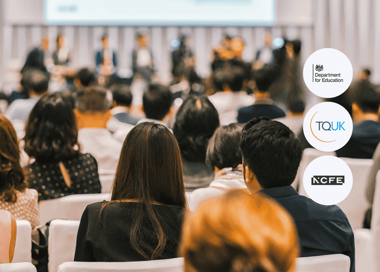 Audience seated in rows facing a blurred panel of speakers at a formal indoor event or conference.