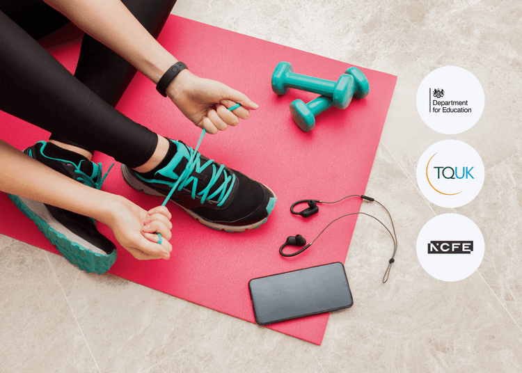 Person tying teal shoelaces on black trainers while sitting on a red exercise mat beside dumbbells, earphones, and a phone.