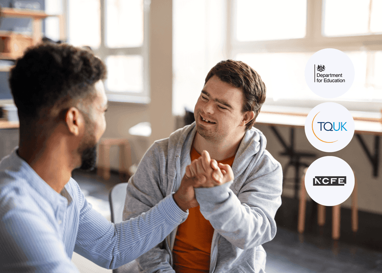 Two people sitting in a bright room, smiling and clasping hands in a supportive gesture during a casual conversation.