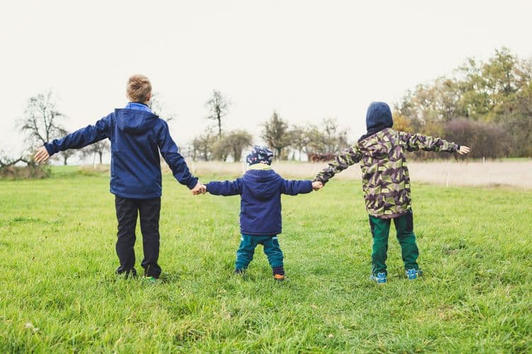 Three children holding hands and walking through a grassy field, representing safe and supportive environments in the Allergy Awareness for Those Working with Children course.