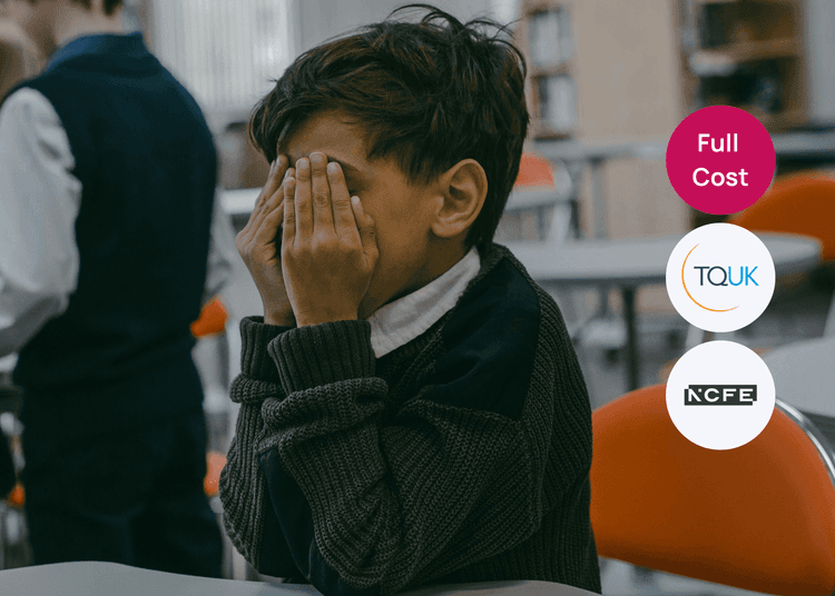 Child sitting with hands over his face in a classroom, highlighting signs educators may notice during safeguarding concerns. Young boy sitting at a classroom table with his hands covering his face, appearing withdrawn.