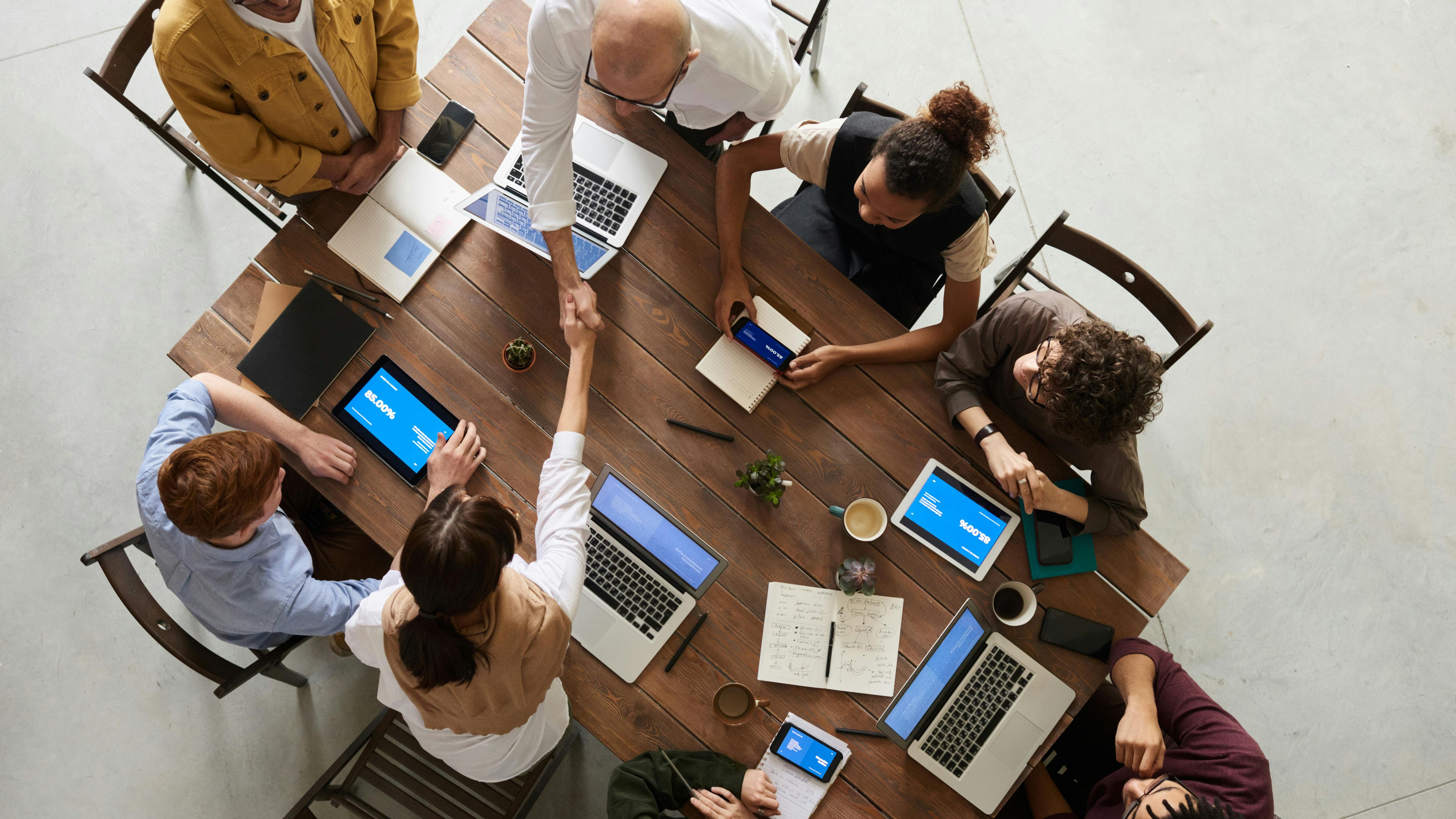 A group of office workers sat around a brown desk with open laptops