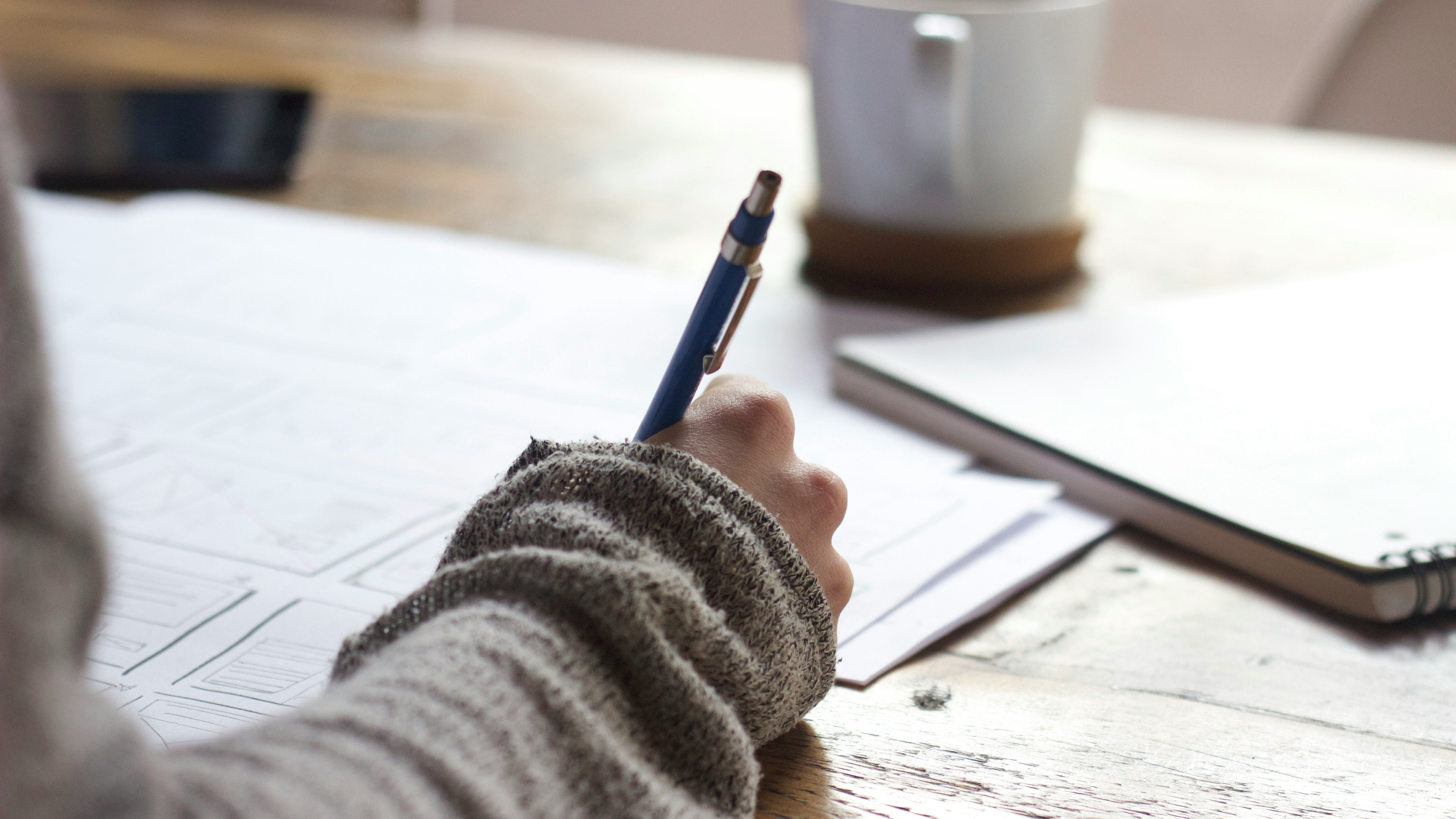 A university student studies at their desk, taking notes with a coffee next to them